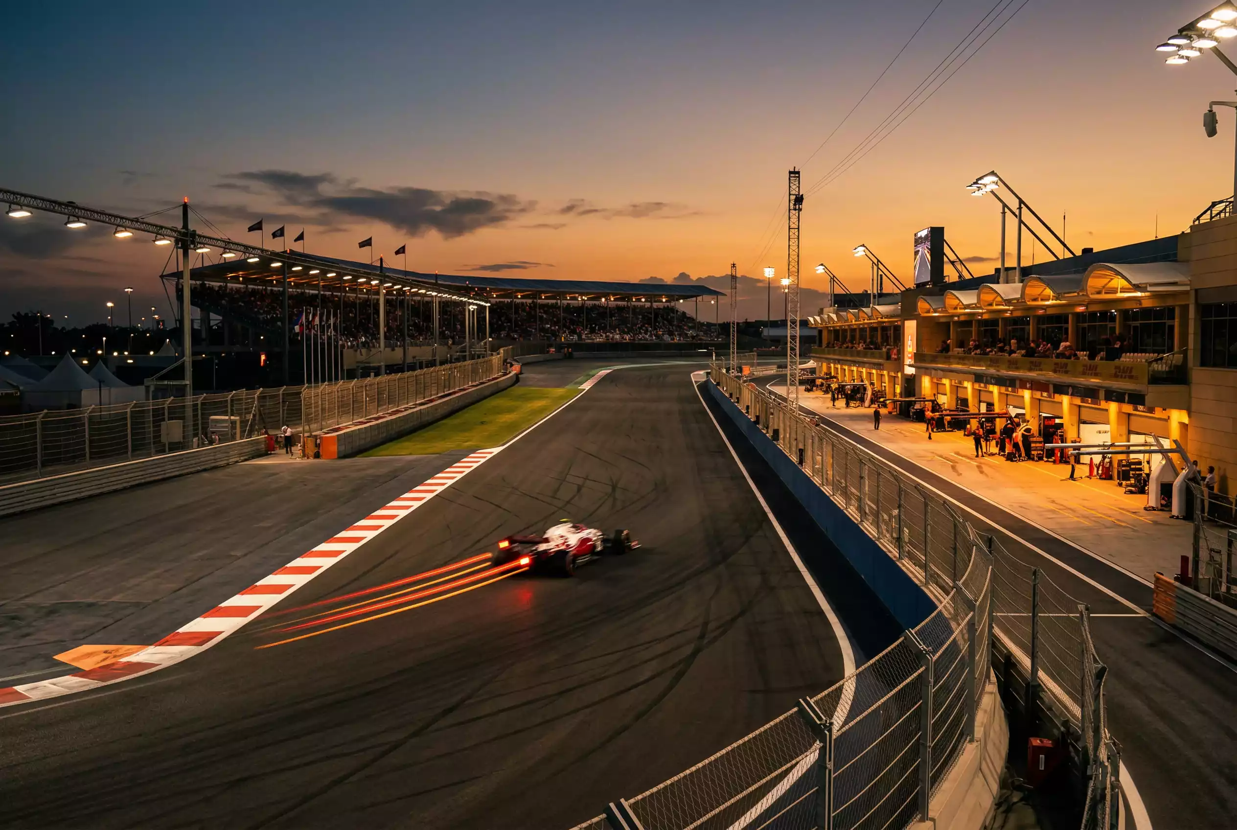 Formel 1 Rennstrecke bei Abenddämmerung mit beleuchteter Boxengasse und Flutlichtmasten