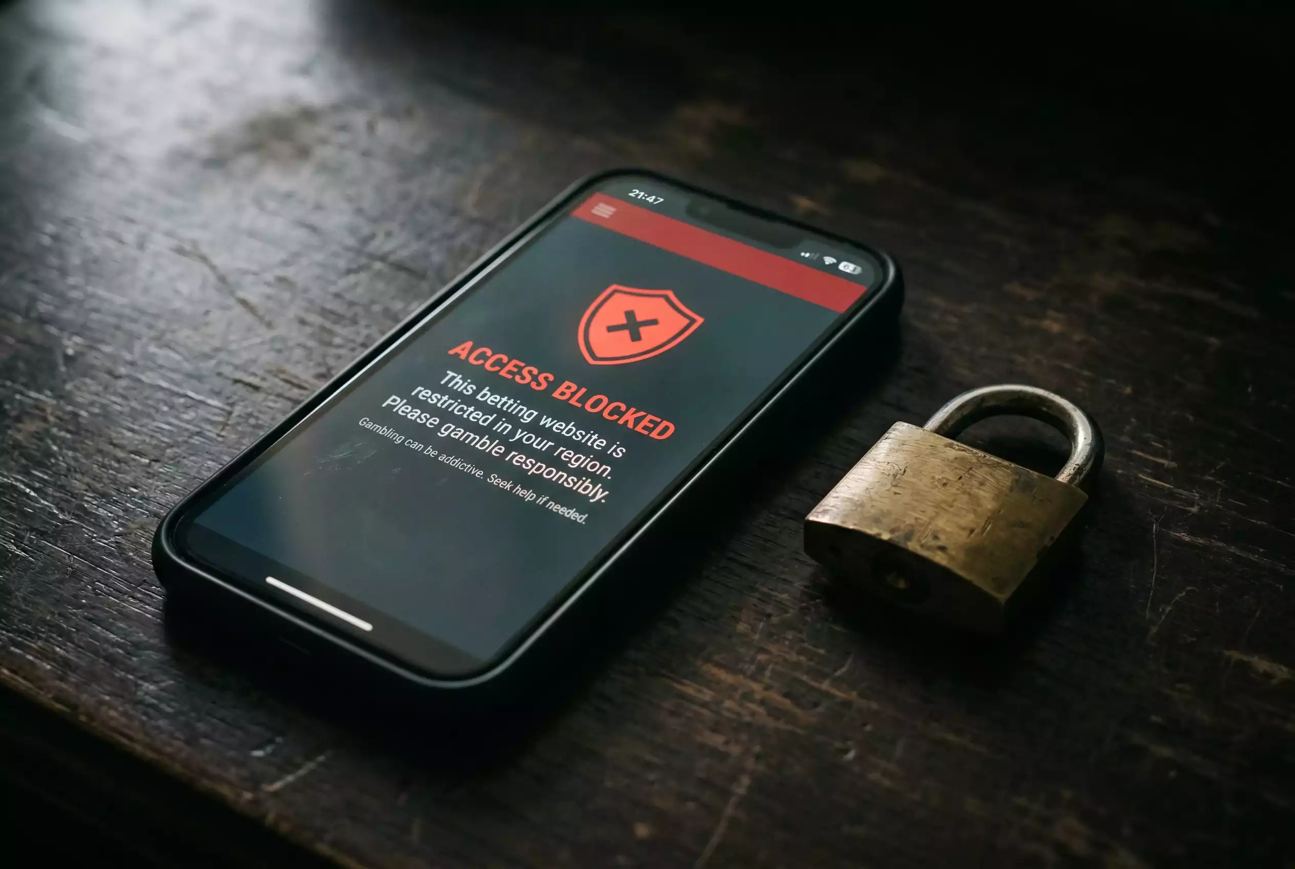 Smartphone mit einer gesperrten Wettseite und einem Warnsymbol auf dem Bildschirm, daneben ein Vorhängeschloss